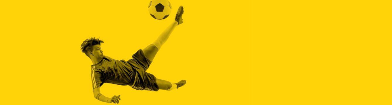 Soccer player jumping mid-air kicking a soccer ball over a yellow background.