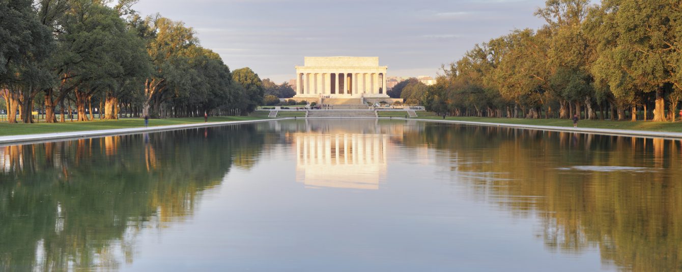 Photo of Lincoln Memorial from a distance, bookended by trees with the memorial and trees reflected over a pond